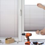 Man installing gray pleated blinds on the window with screwdriver